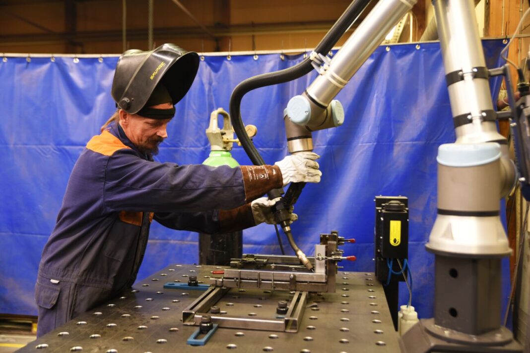 A man with protective gloves an a helmet positioning a cobot to prepare it to weld. 